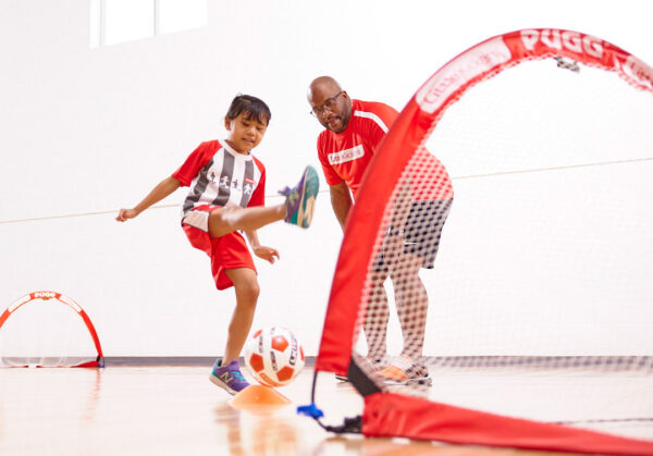 child scoring goal with coach cheering